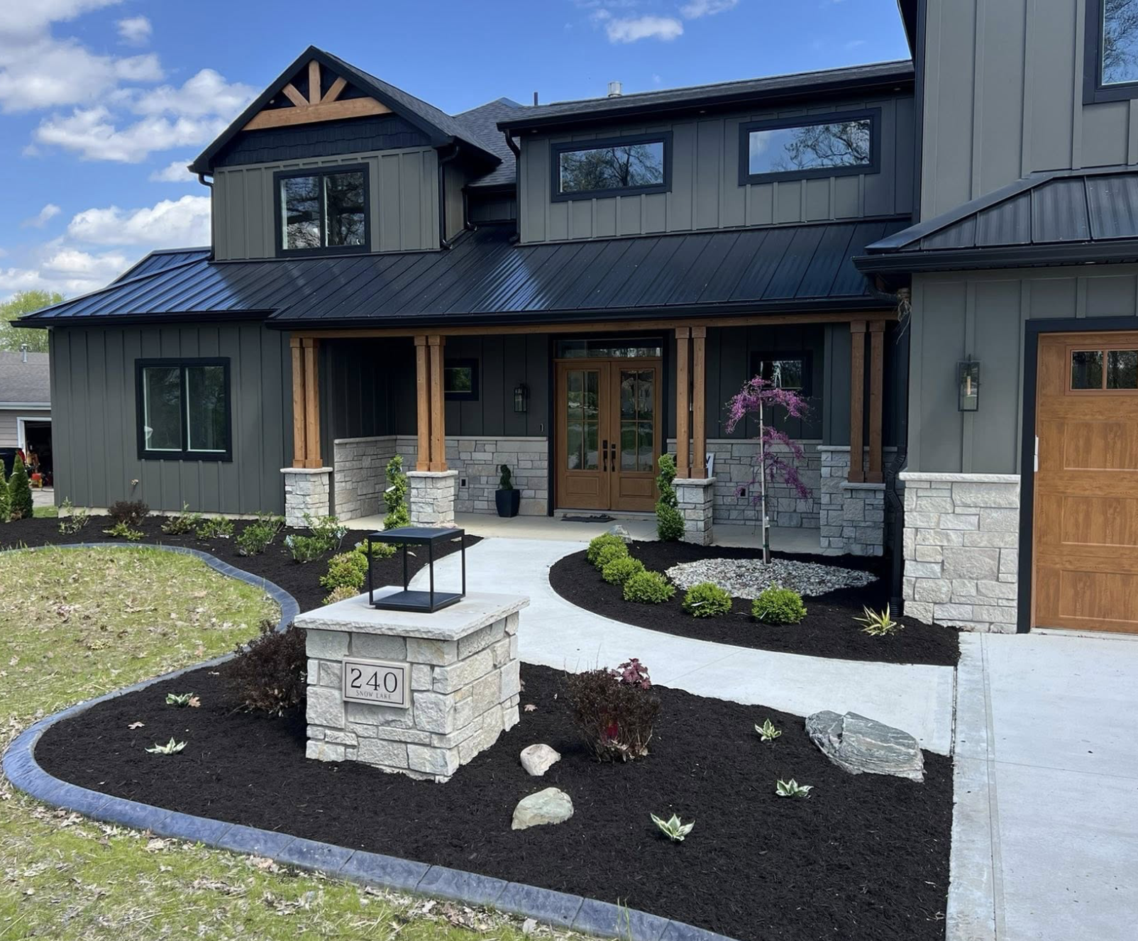 Modern dark-sided home with custom Strongscape landscaping — fresh mulch beds, stone borders, and a custom stone address pillar