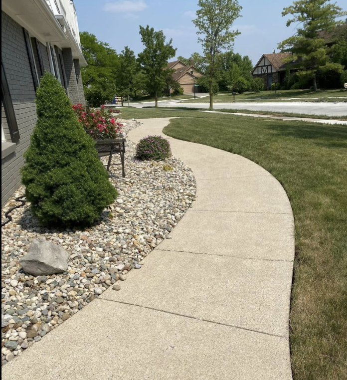 Landscaped walkway with decorative stone bed, manicured shrubs, and a clean curved concrete path