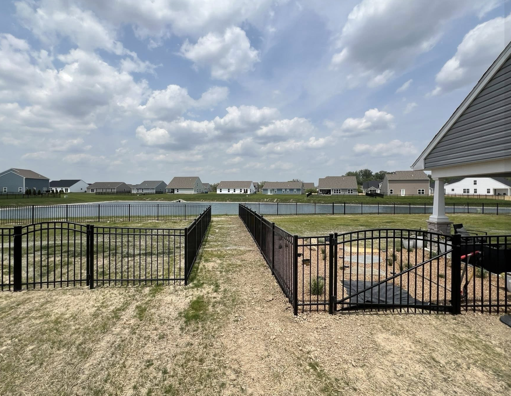Black ornamental aluminum fence with a matching gate bordering a backyard overlooking a pond